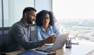 A man and a woman in business attire looking at a laptop screen