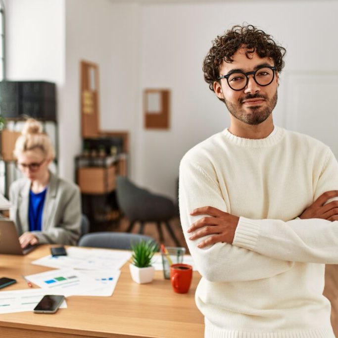 A young businessman posing leaning against his desk