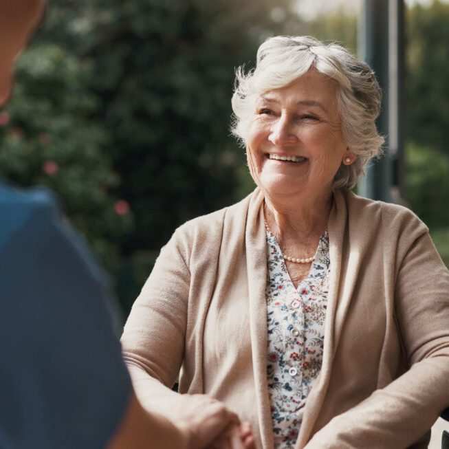 An elderly patient sits holding hands with her nurse